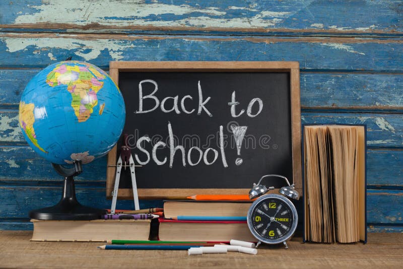 Globe, alarm clock, pencils, chalk, books and slate with back to school text against blue wooden background. Globe, alarm clock, pencils, chalk, books and slate with back to school text against blue wooden background