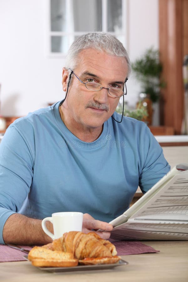 Jornal da leitura do homem sênior no pequeno almoço foto de stock Jornal da leitura do homem sênior no pequeno almoço foto de stock