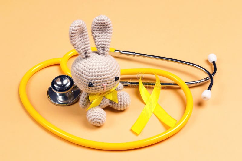 Jouet pour enfants avec un ruban d'or de la sensibilisation au cancer d'enfance et stéthoscope sur le fond jaune