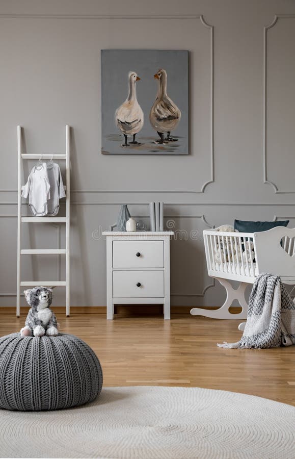 Jouet sur le pouf gris dans la chambre à coucher à la mode de bébé avec le berceau et les meubles en bois blancs, vraie photo ave photos stock Jouet sur le pouf gris dans la chambre à coucher à la mode de bébé avec le berceau et les meubles en bois blancs, vraie photo ave photos stock