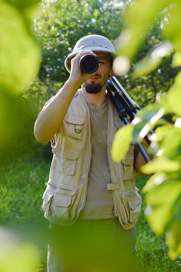 Journey on safari tour: portrait of tourist or exploring scientist male in pith helmet having fun observing looking through scope