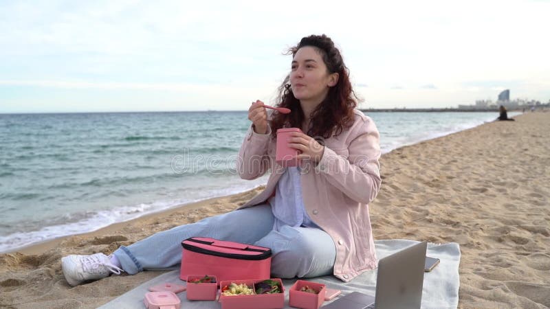 Jovem almoçando na praia comendo sopa de plástico rosa-recipiente.