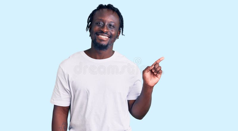 Young african american man with braids wearing casual white tshirt with a big smile on face, pointing with hand finger to the side looking at the camera. Young african american man with braids wearing casual white tshirt with a big smile on face, pointing with hand finger to the side looking at the camera