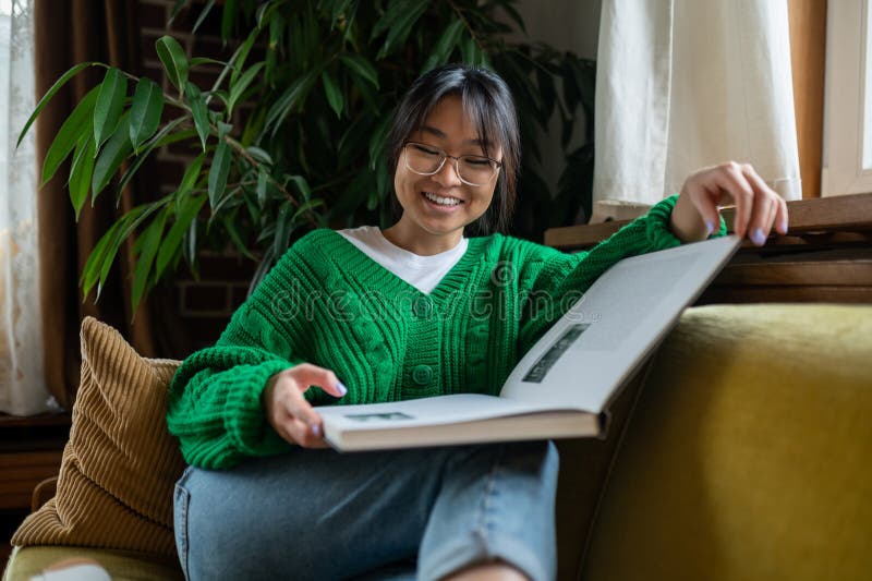 Jovem asiática com um livro grande sentado no sofá imagens de stock royalty free