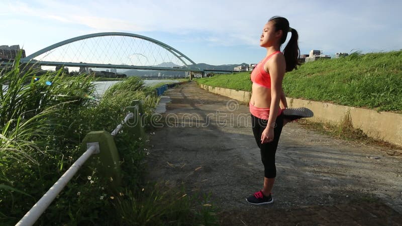 Jovem asiática que se estende antes de uma corrida perto do rio na cidade de taipe