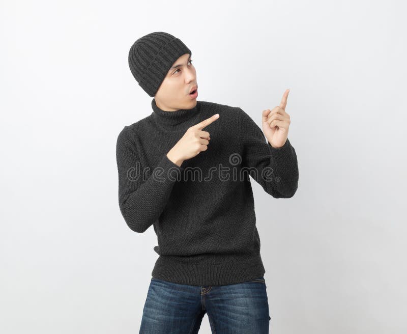 Young handsome asian man wearing grey sweater and beanie pointing to the side with fingers to present a product or an idea on white background. Young handsome asian man wearing grey sweater and beanie pointing to the side with fingers to present a product or an idea on white background