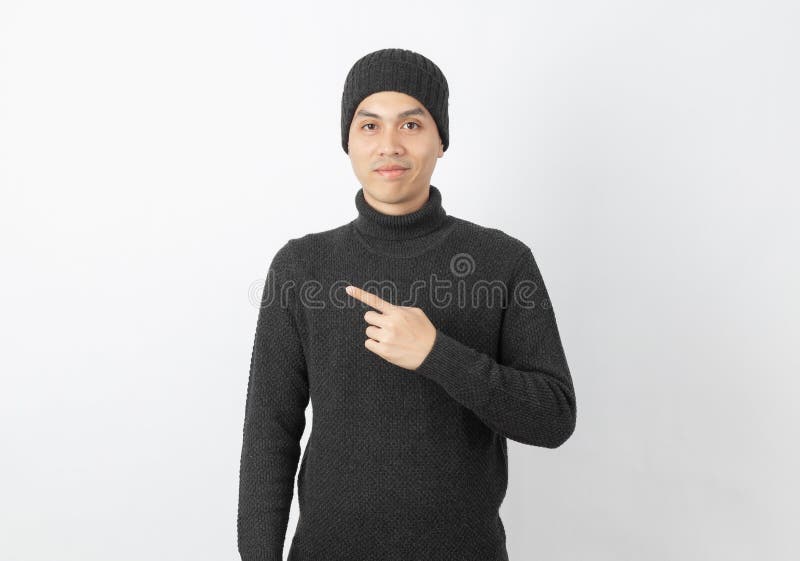 Young handsome asian man wearing grey sweater and beanie pointing to the side with fingers to present a product or an idea on white background. Young handsome asian man wearing grey sweater and beanie pointing to the side with fingers to present a product or an idea on white background
