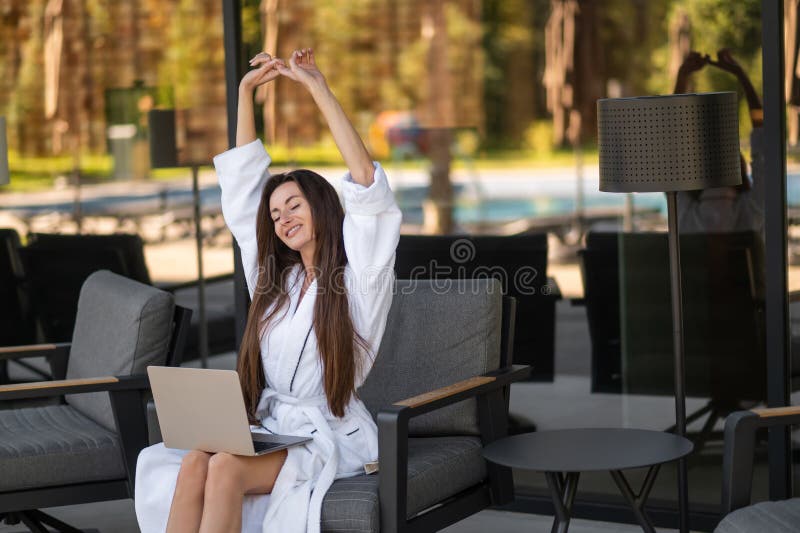 Jovem atraente de roupão branco sentada com um portátil foto de stock