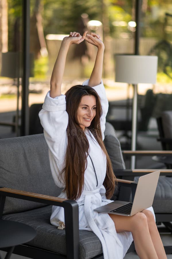 Jovem atraente de roupão branco sentada com um portátil imagem de stock