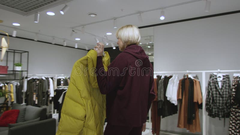 Jovem atraente está examinando uma jaqueta na loja de roupas, tiro de rastreamento, 360 graus