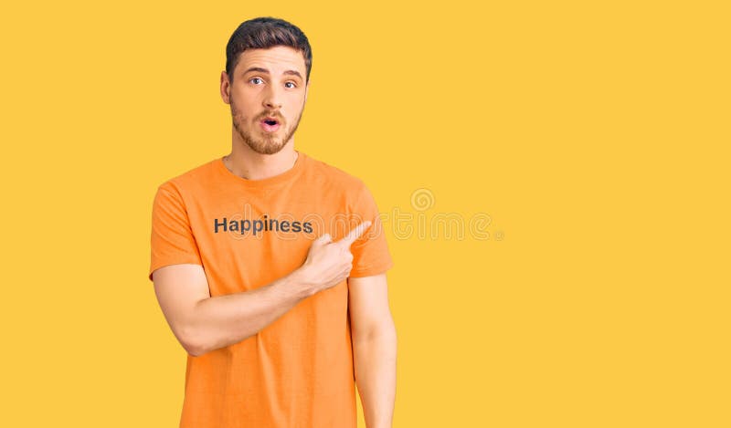 Handsome young man with bear wearing tshirt with happiness word message surprised pointing with finger to the side, open mouth amazed expression. Handsome young man with bear wearing tshirt with happiness word message surprised pointing with finger to the side, open mouth amazed expression