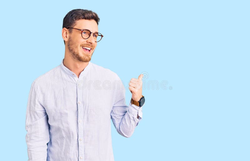 Handsome young man with bear wearing elegant business shirt and glasses smiling with happy face looking and pointing to the side with thumb up. Handsome young man with bear wearing elegant business shirt and glasses smiling with happy face looking and pointing to the side with thumb up