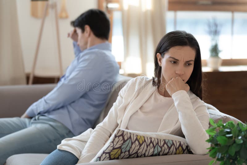 Jovem casal nervoso sentado no sofá mantendo silêncio após discussão