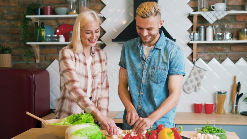 Jovem casal sorrindo cozinhando refeição vegetariana na cozinha em casa