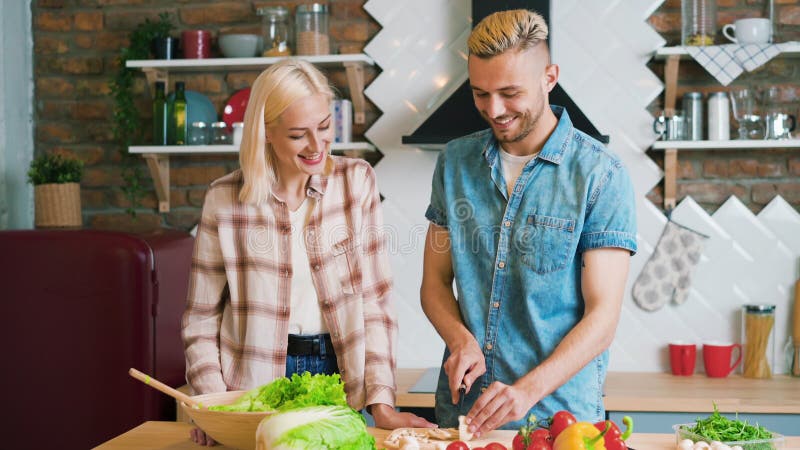 Jovem casal sorrindo cozinhando refeição vegetariana na cozinha em casa