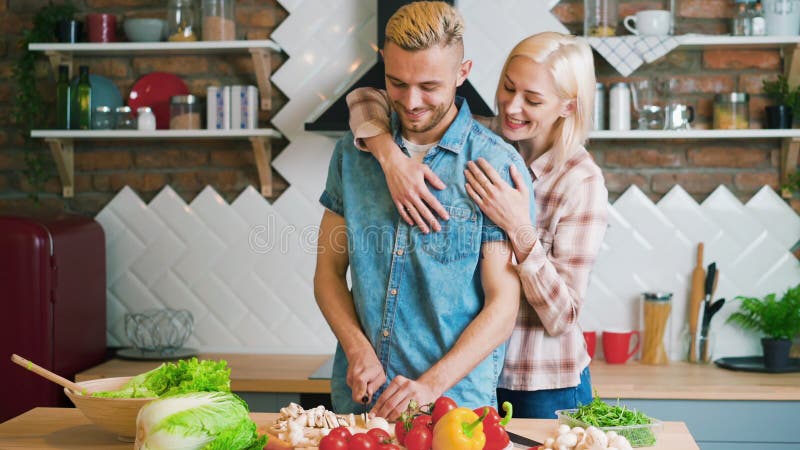 Jovem casal sorrindo cozinhando refeição vegetariana na cozinha em casa