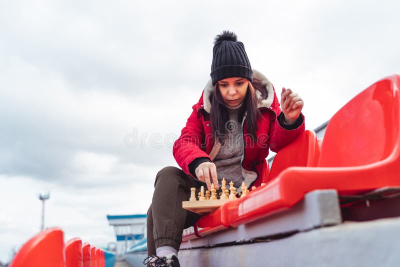 Jovem em roupas de inverno joga xadrez sentado nas