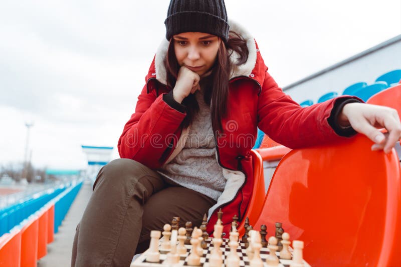 Jovem em roupas de inverno joga xadrez sentado nas