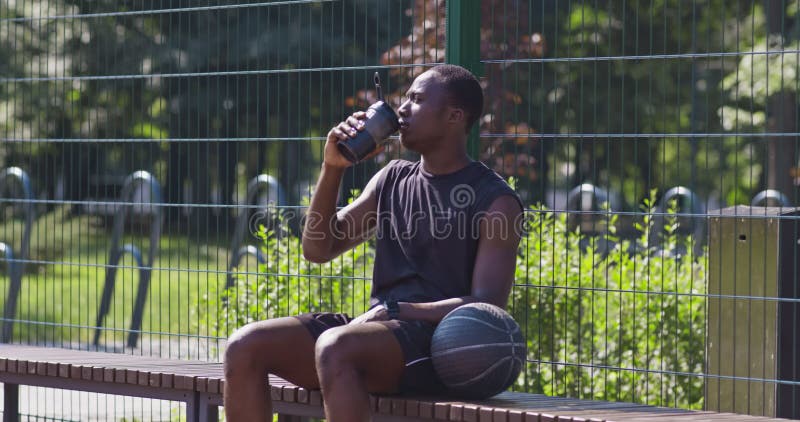 Jovem jogador de basquete feliz sentado no parque com uma toalha