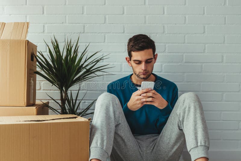 Jovem em casa com telefone celular e caixas móveis fotos de stock