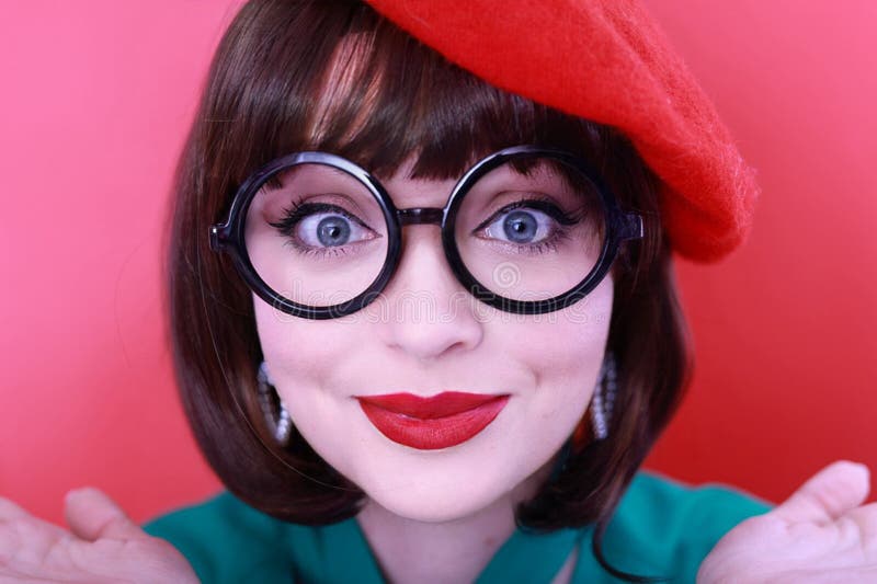 Young happy woman 30 years old wearing glasses, she wears a green grunt and a red hat, shows emotions, celebrates, clenching her fists, says yes, isolated on a plain red background, studio portrait. People lifestyle concept. Young happy woman 30 years old wearing glasses, she wears a green grunt and a red hat, shows emotions, celebrates, clenching her fists, says yes, isolated on a plain red background, studio portrait. People lifestyle concept