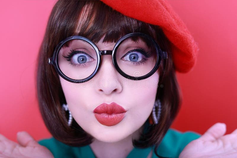 Young happy woman 30 years old wearing glasses, she wears a green grunt and a red hat, shows emotions, celebrates, clenching her fists, says yes, isolated on a plain red background, studio portrait. People lifestyle concept. Young happy woman 30 years old wearing glasses, she wears a green grunt and a red hat, shows emotions, celebrates, clenching her fists, says yes, isolated on a plain red background, studio portrait. People lifestyle concept