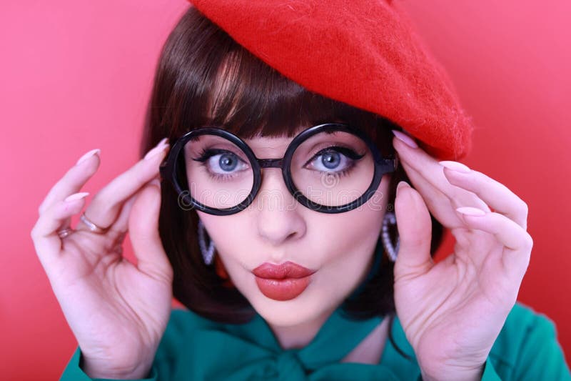 Young happy woman 30 years old wearing glasses, she wears a green grunt and a red hat, shows emotions, celebrates, clenching her fists, says yes, isolated on a plain red background, studio portrait. People lifestyle concept. Young happy woman 30 years old wearing glasses, she wears a green grunt and a red hat, shows emotions, celebrates, clenching her fists, says yes, isolated on a plain red background, studio portrait. People lifestyle concept