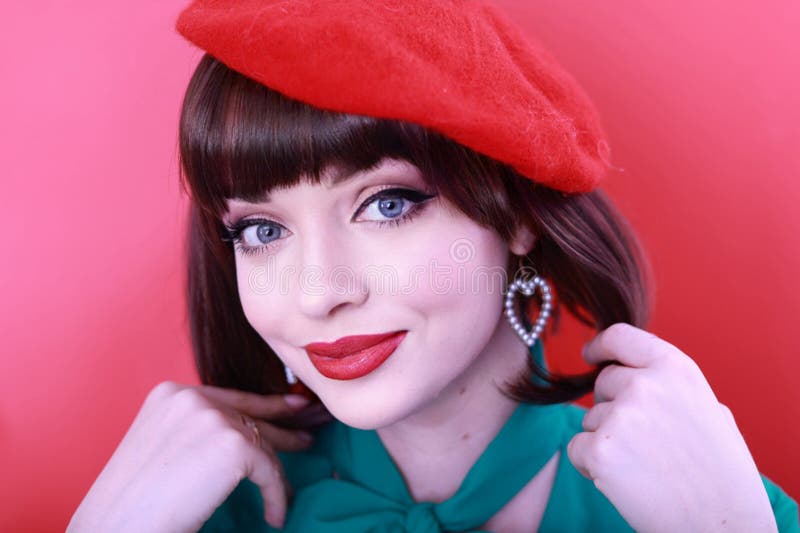 Young happy woman 30 years old wearing glasses, she wears a green grunt and a red hat, shows emotions, celebrates, clenching her fists, says yes, isolated on a plain red background, studio portrait. People lifestyle concept. Young happy woman 30 years old wearing glasses, she wears a green grunt and a red hat, shows emotions, celebrates, clenching her fists, says yes, isolated on a plain red background, studio portrait. People lifestyle concept