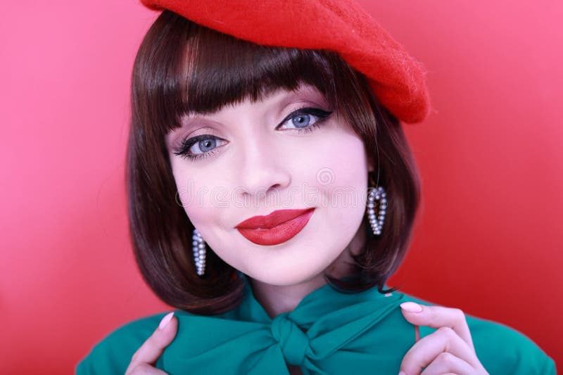 Young happy woman 30 years old wearing glasses, she wears a green grunt and a red hat, shows emotions, celebrates, clenching her fists, says yes, isolated on a plain red background, studio portrait. People lifestyle concept. Young happy woman 30 years old wearing glasses, she wears a green grunt and a red hat, shows emotions, celebrates, clenching her fists, says yes, isolated on a plain red background, studio portrait. People lifestyle concept