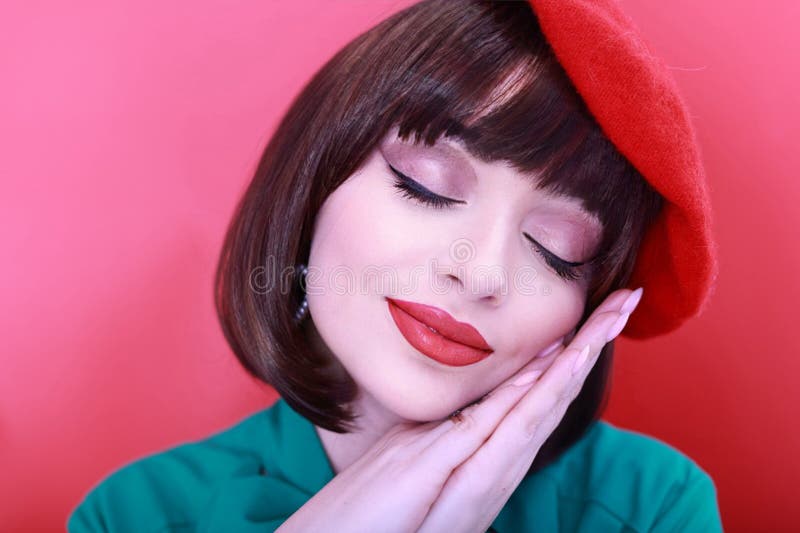 Young happy woman 30 years old wearing glasses, she wears a green grunt and a red hat, shows emotions, celebrates, clenching her fists, says yes, isolated on a plain red background, studio portrait. People lifestyle concept. Young happy woman 30 years old wearing glasses, she wears a green grunt and a red hat, shows emotions, celebrates, clenching her fists, says yes, isolated on a plain red background, studio portrait. People lifestyle concept