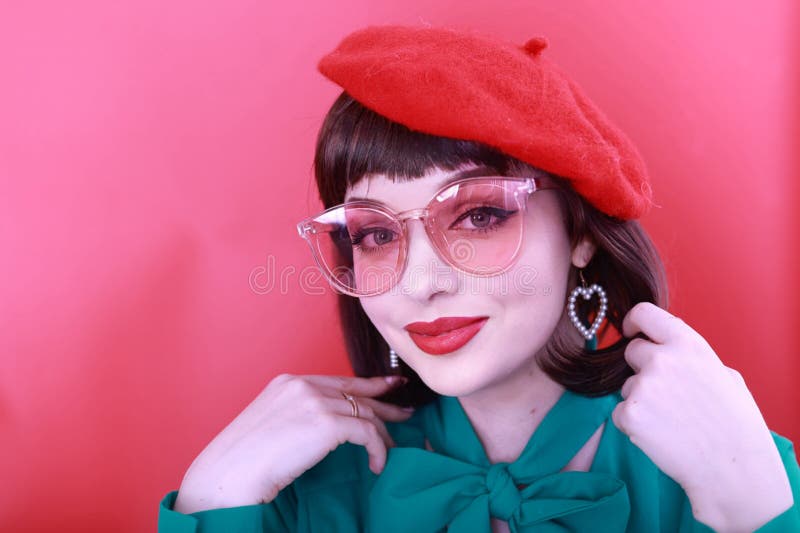 Young happy woman 30 years old wearing glasses, she wears a green grunt and a red hat, shows emotions, celebrates, clenching her fists, says yes, isolated on a plain red background, studio portrait. People lifestyle concept. Young happy woman 30 years old wearing glasses, she wears a green grunt and a red hat, shows emotions, celebrates, clenching her fists, says yes, isolated on a plain red background, studio portrait. People lifestyle concept