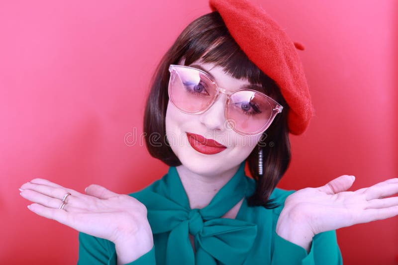 Young happy woman 30 years old wearing glasses, she wears a green grunt and a red hat, shows emotions, celebrates, clenching her fists, says yes, isolated on a plain red background, studio portrait. People lifestyle concept. Young happy woman 30 years old wearing glasses, she wears a green grunt and a red hat, shows emotions, celebrates, clenching her fists, says yes, isolated on a plain red background, studio portrait. People lifestyle concept