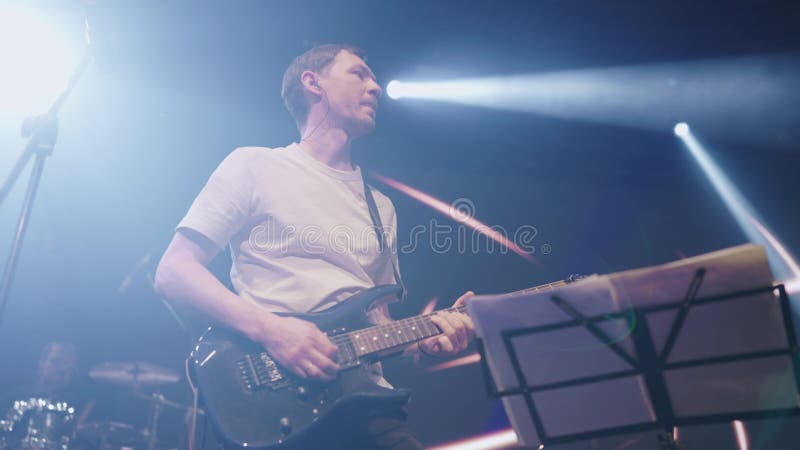 Jovem guitarrista faz parte solo no concerto pop group no clube. movimento lento