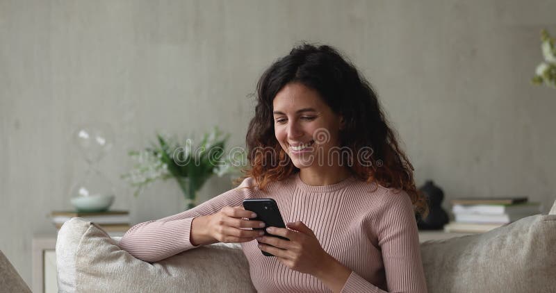 Jovem hispânica sorridente usando smartphone em casa.