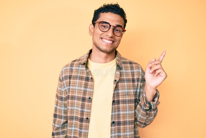 Young handsome hispanic man wearing casual clothes and glasses smiling happy pointing with hand and finger to the side. Young handsome hispanic man wearing casual clothes and glasses smiling happy pointing with hand and finger to the side