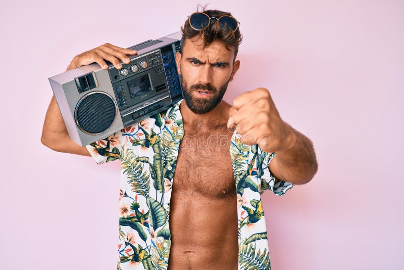 Young hispanic man wearing summer clothes holding boombox, listening to music smiling cheerful pointing with hand and finger up to the side. Young hispanic man wearing summer clothes holding boombox, listening to music smiling cheerful pointing with hand and finger up to the side
