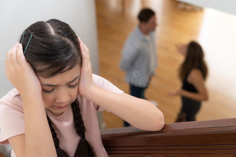 Stressed and unhappy young girl cover her ears blocking sound tension by her parent argument from the stair. Unhealthy family and domestic violence lead to traumatic childhood and anxiety. Synchronos. Stressed and unhappy young girl cover her ears blocking sound tension by her parent argument from the stair. Unhealthy family and domestic violence lead to traumatic childhood and anxiety. Synchronos