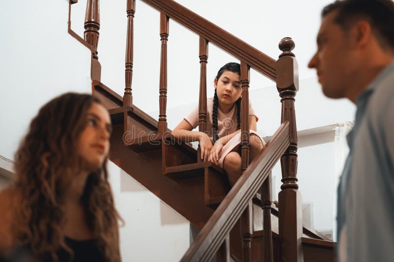 Stressed and unhappy young girl watch her parent arguing from the stair. Domestic violence at home and traumatic childhood develop to depression and anxiety. Unhealthy family concept. Synchronos. Stressed and unhappy young girl watch her parent arguing from the stair. Domestic violence at home and traumatic childhood develop to depression and anxiety. Unhealthy family concept. Synchronos