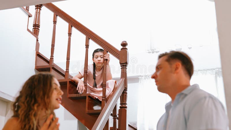 Stressed and unhappy young girl watch her parent arguing from the stair. Domestic violence at home and traumatic childhood develop to depression and anxiety. Unhealthy family concept. Synchronos. Stressed and unhappy young girl watch her parent arguing from the stair. Domestic violence at home and traumatic childhood develop to depression and anxiety. Unhealthy family concept. Synchronos