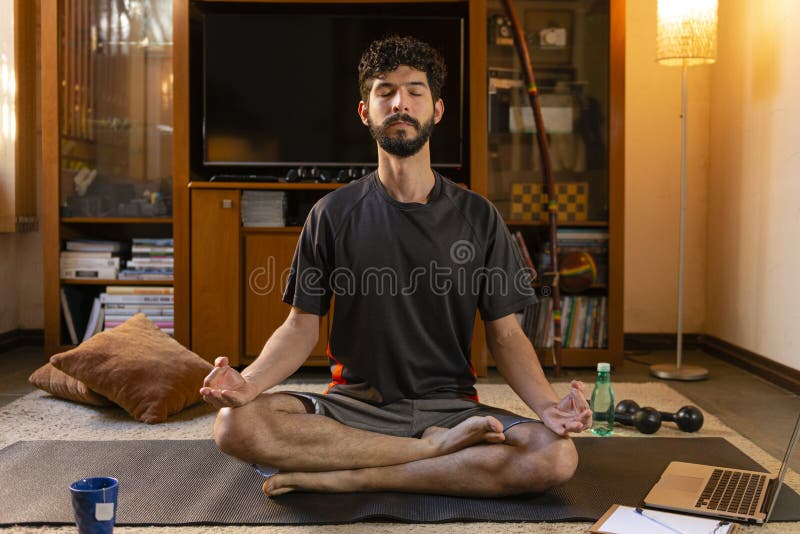 Latin young man meditating, listening to yoga practice lessons through laptop. Sitting in the lotus position. Home yoga concept. Latin young man meditating, listening to yoga practice lessons through laptop. Sitting in the lotus position. Home yoga concept.