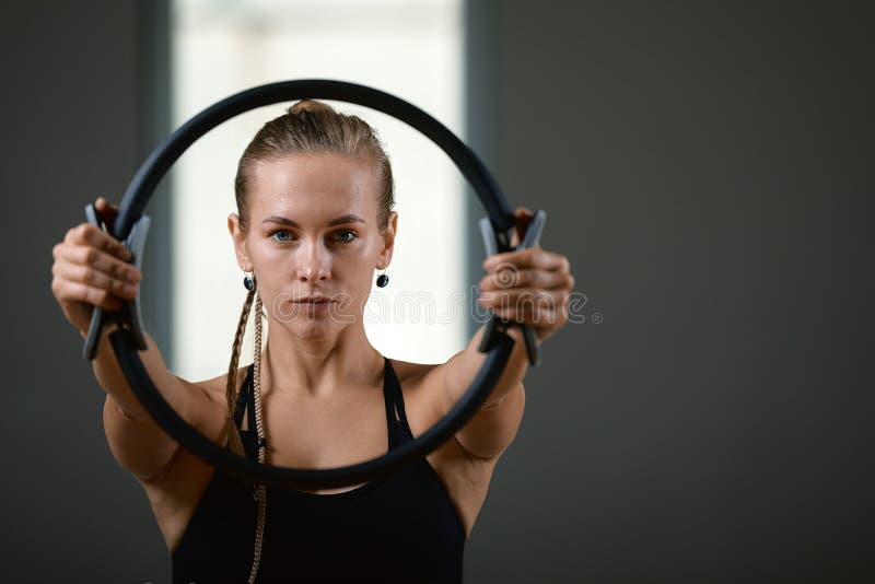 Jovem, linda, garota atlética está fazendo exercícios com o anel Pilates na academia em um fundo cinza Esporte