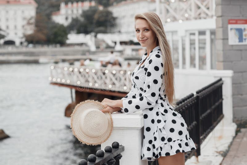 Jovem linda, loira de cabelo comprido, com um vestido branco de verão, uma caminha numa cidade ensolarada foto de stock Jovem linda, loira de cabelo comprido, com um vestido branco de verão, uma caminha numa cidade ensolarada foto de stock