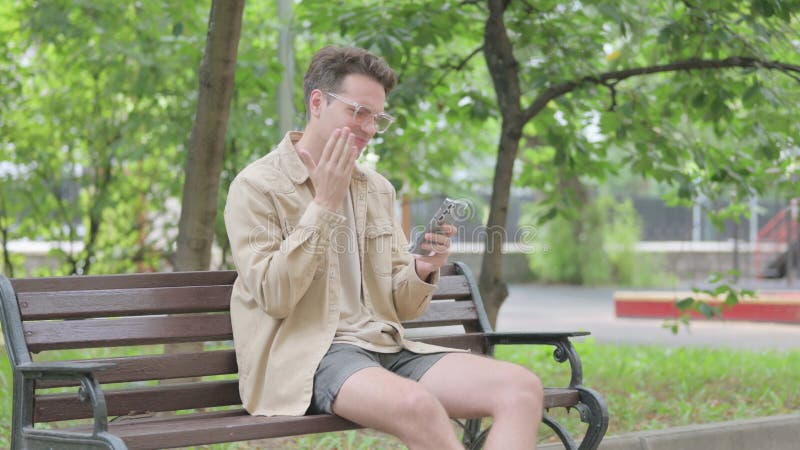 Jovem moderno enfrentando perda no smartphone enquanto sentado no banco