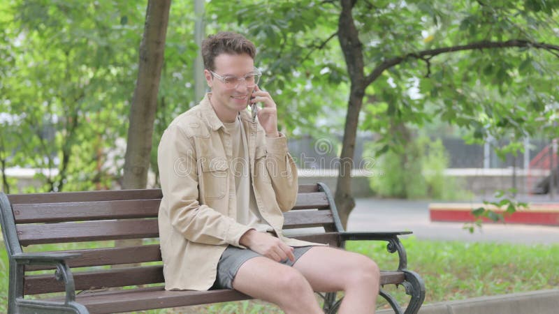 Jovem moderno falando ao telefone enquanto sentado no banco