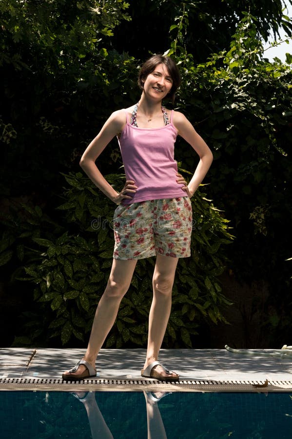 Jovem mulher alegre feliz que está no jardim perto da piscina foto de stock Jovem mulher alegre feliz que está no jardim perto da piscina foto de stock
