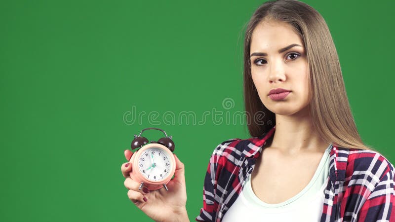 Jovem mulher bonita que aponta no despertador que olha sério imagem de stock Jovem mulher bonita que aponta no despertador que olha sério imagem de stock