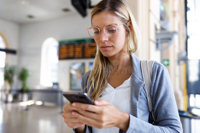 Jovem mulher bonita que texting com seu telefone celular no salão de estação de caminhos de ferro fotos de stock Jovem mulher bonita que texting com seu telefone celular no salão de estação de caminhos de ferro fotos de stock