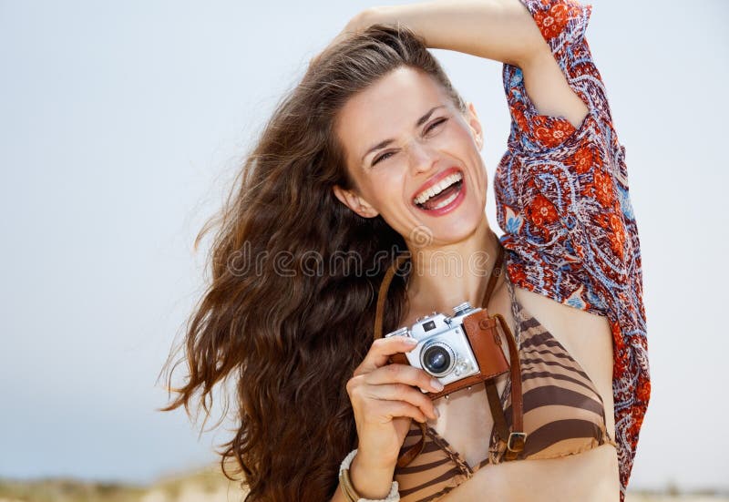 Jovem mulher boêmia de sorriso com a câmera retro da foto na praia