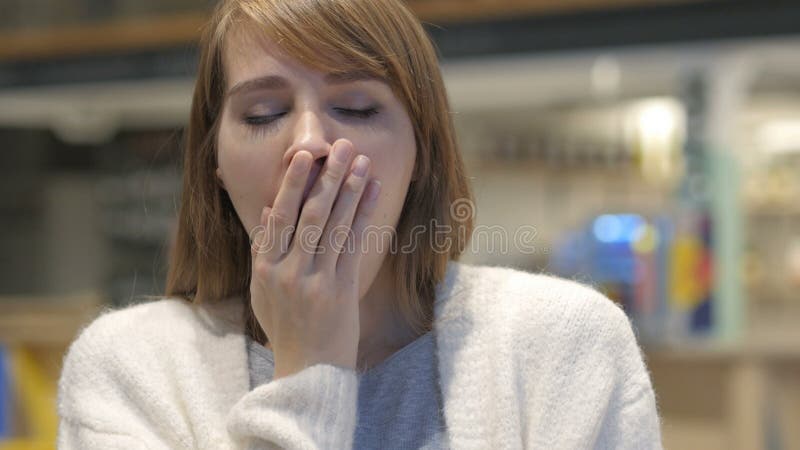 Jovem mulher cansado que boceja no café, interno