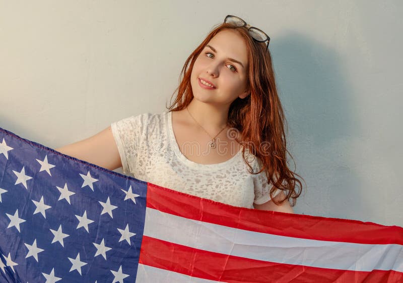 A jovem mulher com a bandeira americana nas mãos que olham o vintage da câmera coloriu a imagem imagem de stock A jovem mulher com a bandeira americana nas mãos que olham o vintage da câmera coloriu a imagem imagem de stock